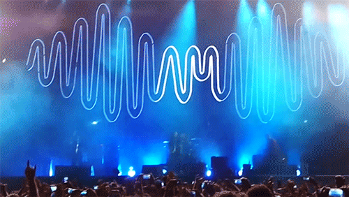 símbolo da banda arctic monkeys no fundo de um show, em azul, e uma mãos se levantando na frente fazendo o símbolo do rock
